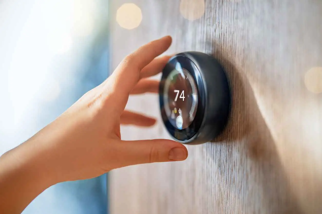 A hand reaching towards a smart thermostat to adjust the temperature in the home