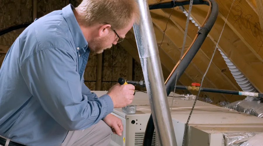 Hvac Tech Looking Over A Furnace In The Attic (1)